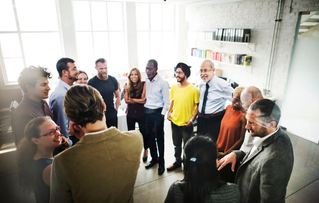 Equipe com diversos funcionários em pé, conversando entre si em ambiente de trabalho.